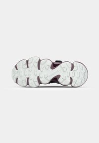Sneaker sole with a textured white rubber surface, featuring a prominent purple midsole, and defined traction patterns for grip.