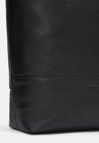 Sac fourre-tout en cuir noir avec une finition texturée, de forme rectangulaire et des détails de couture visibles le long des bords et de la base.