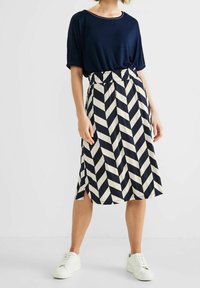 Laivastonsininen t-paita lyhyillä hihoilla yhdistettynä polvenpituiseen, laivastonsinisen ja kermanvärisen viiru-kuosiseksi hameeksi, jossa on joustava vyötärö.