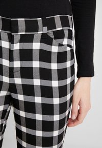 Pantalons à carreaux noir et blanc avec une taille ajustée, dotés d'une poche avant et d'une texture lisse. Détails de couture visibles à la taille.