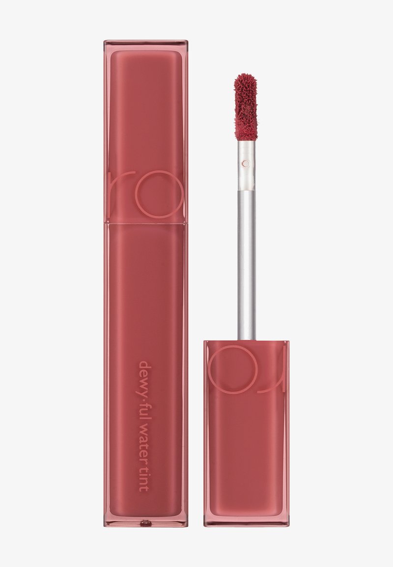 Rouge à lèvres liquide mat dans un tube rectangulaire transparent avec un applicateur flou. Le capuchon présente des accents roses texturés et une marque en rose clair.