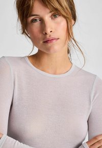 Cămașă lungă cu mânecă dintr-un material subțire, transparent, de culoare gri deschis, cu decolteu rotund și mâneci fără cusături. Textura subtilă este vizibilă.