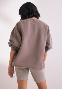 Felpa oversize con interno in pile di un taupe tenue, caratterizzata da spalle scese e polsini a costine, abbinata a pantaloni bike a costine di un grigio chiaro.