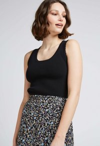 Débardeur noir à côtes avec un décolleté arrondi, associé à une jupe à motif floral présentant des fleurs multicolores sur un fond sombre.