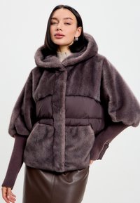 Umělá kožešinová bunda v tmavě šedé barvě, s nadýchaným designem a kapucí. Obsahuje elastické rukávy, přední kapsy a měkkou texturu.