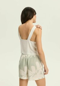 Biała bezrękawnikowa bluzka z szerokimi ramiączkami, zestawiona z miętowymi szortami z dużym białym wzorem kwiatowym. Gładka tekstura, luźny krój.