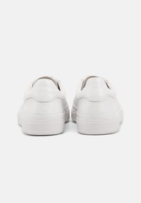 Bílé kožené tenisky s hladkým povrchem, zaoblenými patami, texturovanou podrážkou a minimalistickým designem bez viditelného brandingu.
