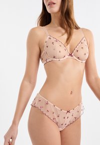 Jasnoróżowy przezroczysty komplet bielizny z falistymi krawędziami, haftem kwiatowym w kolorze fioletowym i różowym, składający się z trójkątnego biustonosza i pasujących majtek.