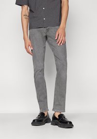 Grå denimjeans med smal passform og standard fem-lommers design, kombinert med sorte loafers og en kortermet rutete skjorte.