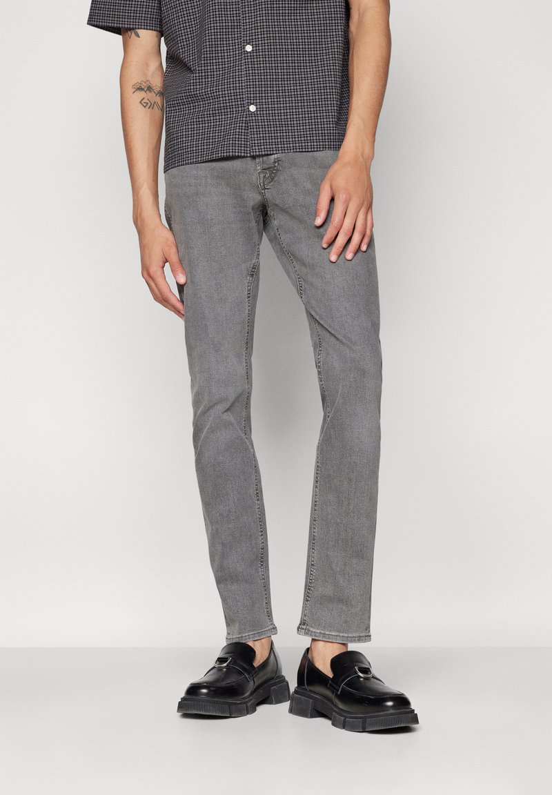 Grå denimjeans med smal passform og standard fem-lommers design, kombinert med sorte loafers og en kortermet rutete skjorte.