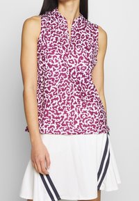 Bezramenný top v purpurové barvě s bílým abstraktním vzorem, s límečkem a půl-knoflíkovou légou. V kombinaci s bílou sukní s námořnickými pruhy.