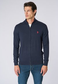 Cardigan zip-up navy con colletto alto, polsini e orlo a coste, caratterizzato da un piccolo logo rosso sul petto. Realizzato in un morbido tessuto testurizzato.