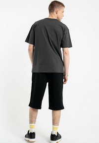 Czarne bawełniane szorty i szary bawełniany t-shirt z krótkimi rękawami oraz luźnym krojem. Uzupełnione żółtymi skarpetami w paski i ciemnymi sneakersami.