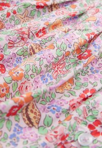 Tkanina z motivi cvetja in listov v živahnih barvah na svetlem ozadju, z mehko teksturo in nabranimi gubami.