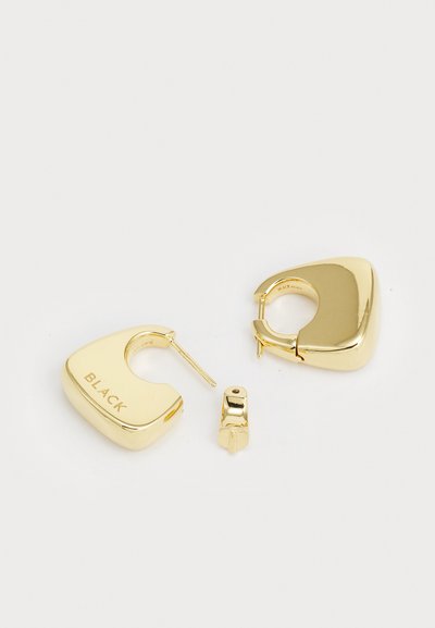 Pendientes de aro en tono dorado con un diseño grueso y redondeado. Un pendiente tiene grabado "BLACK"; acabado suave y brillante con cierre de clip.