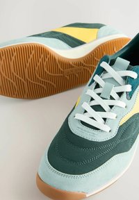 Sneakers da uomo dal design teal e giallo, realizzati in materiali scamosciati e mesh, con lacci bianchi e suola in gomma con un motivo testurizzato.