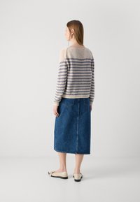 Gebreide trui in beige en lichtblauwe strepen, gecombineerd met een blauwe denim midi rok. Schoenen zijn lichtbeige flats. Achteraanzicht van de outfit.