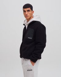 Giacca in pile nera con finitura testurizzata, dotata di una tasca con zip nera a contrasto e una felpa con cappuccio grigia sottostante. Vestibilità regolata.