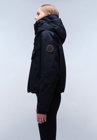 Giacca nera isolante con colletto alto, tasche con zip, patch del logo sulla manica e finitura opaca. Inclusi chiusure in velcro.
