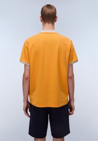 Kortærmet t-shirt i strålende gul bomuld med en struktureret overflade, med en kontrasterende lysbeige krave og manchetter, båret med navy shorts.