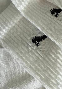 Weiße Socken mit gerippter Textur und schwarzem gesticktem Design, das eine kleine Tiersilhouette zeigt. Der Stoff wirkt weich und dehnbar.