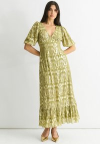 Maxi dress in light green with a shiny, textured finish. Features puff sleeves, a deep V-neck, and a ruffled hem for added detail.