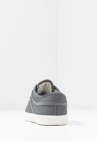 Sneaker in tela grigia con suola in gomma bianca texturizzata, retro arrotondato e dettagli di cucitura discreti lungo i lati.