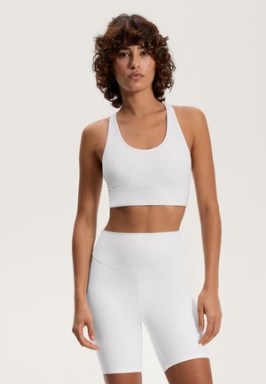 Valkoinen urheilullinen crop-top ja korkeavyötäröiset shortsit, molemmat sileää, venyvästä kankaasta. Yksinkertainen muotoilu ilman näkyviä kuvioita tai yksityiskohtia.