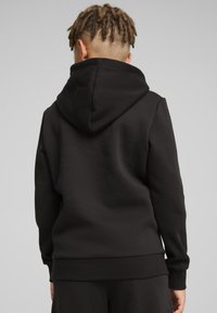 Juodas jaukios medžiagos džemperis su dideliu gobtuvu, raukšlėtomis rankovėmis ir apačia. Lygus tekstūra ir minimalistinis dizainas.