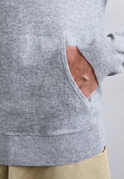 Grauer Strickpullover mit geripptem Saum und Bündchen. Verfügt über eine Seitentasche mit glatter Textur. Der Hintergrund ist neutral.