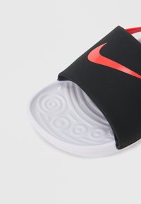 Μαύρο σανδάλι με λουράκι, με γυαλιστερό κόκκινο λογότυπο Nike, λευκή ανάγλυφη σόλα και απαλό λουράκι για άνεση.