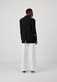 Sacou negru, pe corp, cu un design structurat, mâneci lungi și accente decorative cu nasturi. Asortat cu pantaloni albi, cu talie înaltă, drept.