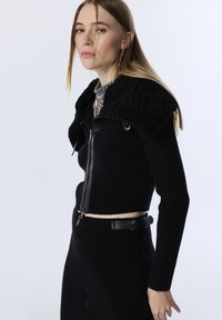 Zwarte geribbelde gebreide trui en rok set met een faux fur kraag, ritsluiting en bijpassende leren ceintuur. Gladde textuur met een getailleerd ontwerp.