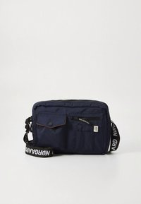 Marineblaue Umhängetasche mit mehreren Vordertaschen, schwarzem Reißverschluss, Klappe mit Druckknopf und schwarzem verstellbarem Riemen mit weißer Beschriftung.