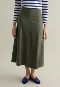 Olive green, A-line skirt made of soft fabric. Features a smooth texture, mid-calf length, and subtle panel detailing. Worn with blue shoes.