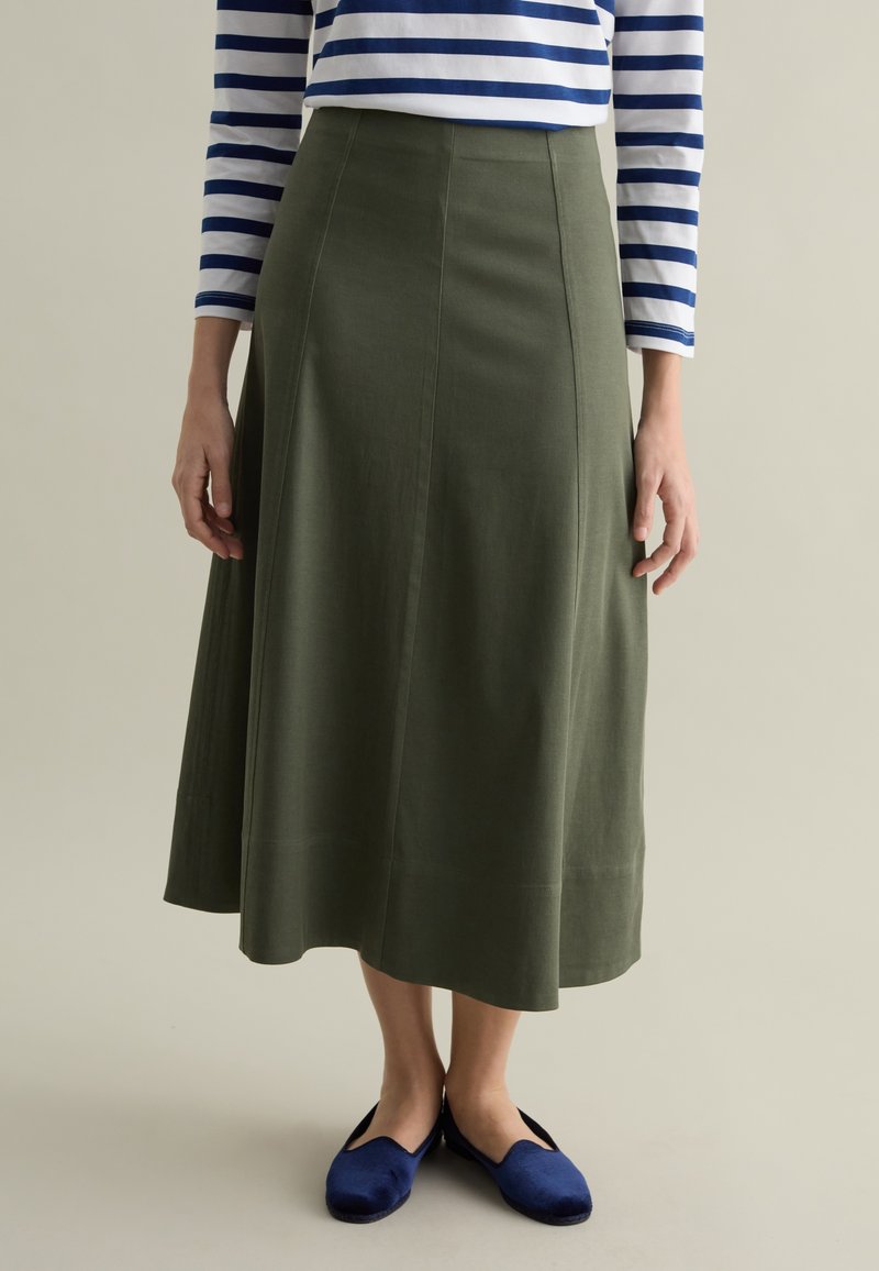 Olive green, A-line skirt made of soft fabric. Features a smooth texture, mid-calf length, and subtle panel detailing. Worn with blue shoes.