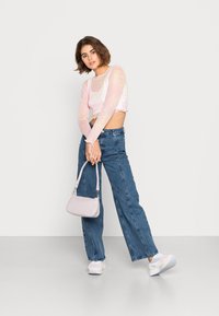 Top cropped de mangas longas rosa claro com um acabamento texturizado, combinado com calças de ganga azuis de cintura alta. Segurando uma pequena mala rosa. Ténis brancos.