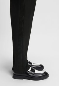 Mustvalged nahast loafer-tüüpi kingad, mida kantakse mustade pükstega, millel on satiinist küljeriba, näidatud külgvaates ühetaustal.