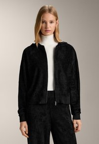 Čierna mikina na zips vyrobená z mäkkej, textúrovanej látky; má kapucňu, rebrované manžety a moderný strih, doplnená o zodpovedajúce čierne nohavice.