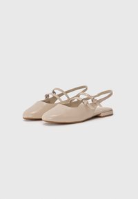 Ballerines à talon plat en cuir verni beige avec un bout pointu, des doubles brides croisées et un petit talon plat.