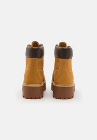 Botas de tornozelo castanhas e bege com parte superior em couro, colarinho acolchoado e sola grossa. Apresenta costuras em contraste e um padrão de pisada robusto.