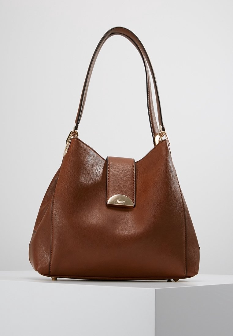 Brown leather handbag with smooth texture, a rounded shape, and a gold hardware accent on the front flap. Features a single strap.