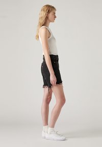 Black denim shorts with frayed hems, high-rise fit, and classic five-pocket design, paired with a white sleeveless top and white sneakers.
