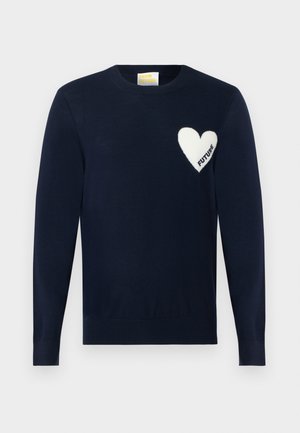 Pull-over bleu marine à col rond avec un écusson blanc en forme de cœur sur le côté gauche de la poitrine, avec le mot « FUTURE » à l'intérieur du cœur.