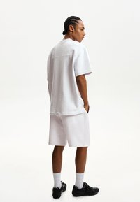 Szürke, oversize t-shirt és passzoló rövidnadrág, puha pamutkeverékből készült, rövid ujjú és laza szabású. Fekete sportcipők egészítik ki a megjelenést.