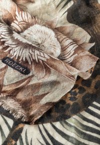 Patterned fabric featuring floral and animal motifs in brown, beige, and black, with a frayed edge and a label reading "ROECKL."