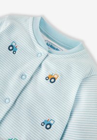 Šviesiai mėlynas kūdikių bodysuit'as su mėlynomis, oranžinėmis ir žaliomis siuvinėtomis traktorių detalėmis. Yra snapeliai ir minkšta medvilnė.
