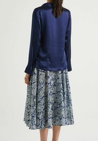 Blusa lunga a maniche con lucido blu navy abbinata a una gonna a campana lunga alla caviglia con un motivo floreale blu e bianco. Materiali texturizzati e svolazzanti.