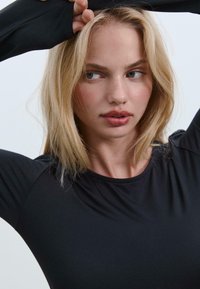Schwarzes Langarmshirt mit Rundhalsausschnitt, aus einem glatten, dehnbarem Stoff gefertigt. Hat eng anliegende Ärmel und ein minimalistisches Design.