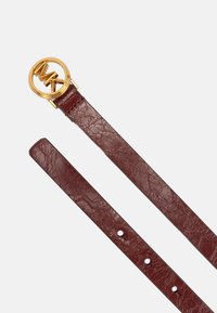 Bordeaux leren riem met een ronde gouden gesp met de initialen "MK." De band heeft een textuur met meerdere verstelgaten.